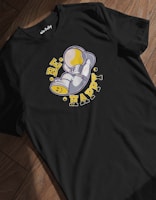 A black t-shirt with an illustrated design of a small space character lying on its side, wearing a helmet, positioned in the center. Surrounding the character are the words 'BE HAPPY' in bold, distressed yellow letters, with small circular accents.