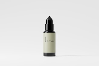 A black and cream-colored dropper bottle displayed against a plain white background. The bottle has a minimalist design with the text 'kanva' printed on it. Shadows are subtly cast beneath the bottle.