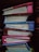 A stack of six thick notebooks or journals with colorful covers is arranged on a dark shelf. The spines are mostly visible, showing some signs of wear. The covers are of different colors including red, blue, and pink.