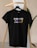 A black t-shirt hangs on a wooden hanger against a light-colored background. The t-shirt bears the text 'ENGINEER KI JAAN LOGE KYA?' in a mix of white, purple, and yellow fonts.