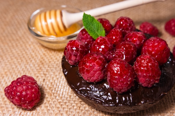 A chocolate cake topped with raspberries and a honey dip