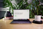 A laptop displaying a webpage titled 'Unlocking the Future of Finance with Ljubljana' is positioned on a wooden table. Surrounding the laptop are green plants, a stack of books, a black object, and a white mug with the word 'webflow' printed on it. The setting appears to be a comfortable workspace or home office.