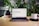 A laptop displaying a webpage titled 'Unlocking the Future of Finance with Ljubljana' is positioned on a wooden table. Surrounding the laptop are green plants, a stack of books, a black object, and a white mug with the word 'webflow' printed on it. The setting appears to be a comfortable workspace or home office.