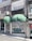 A storefront with two large green awnings, one of which displays the name 'AZE Art & Antique.' Graffiti covers the metal shutters below the awnings, with various tags and phrases. The building features a mix of texture with speckled and smooth surfaces. An air conditioning unit is mounted on the wall above, and a Turkish flag is displayed to the side.