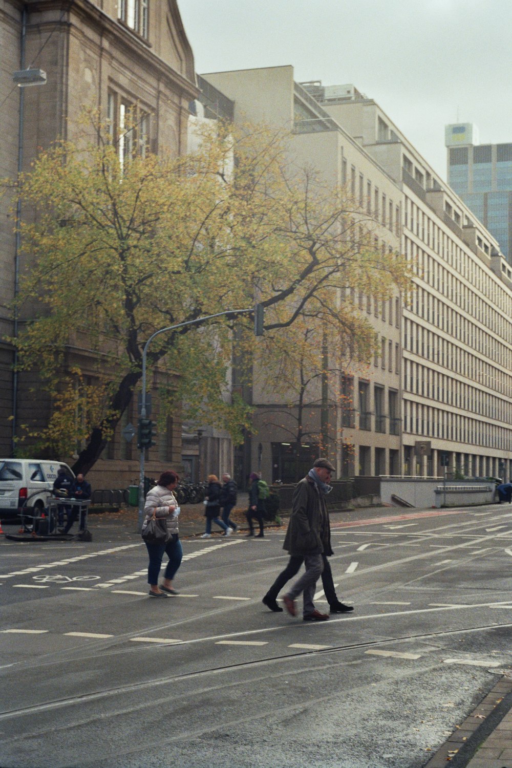 a group of people walking across a street next to tall buildings