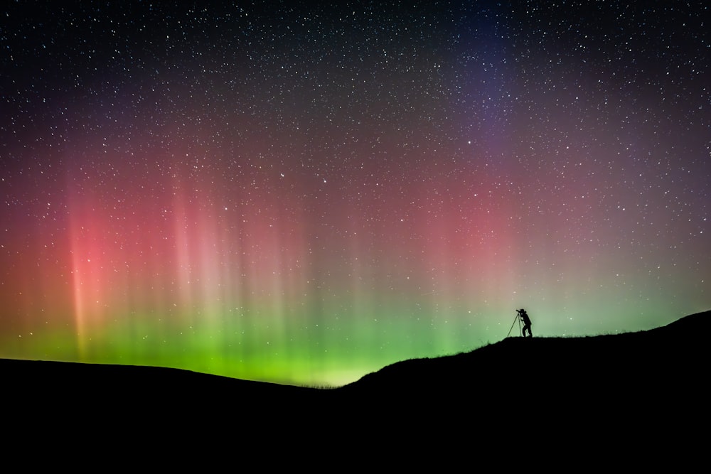 a person standing on top of a hill under a colorful sky