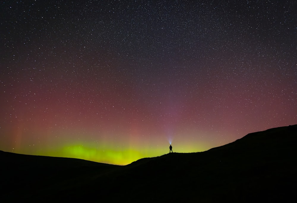 a person standing on top of a hill under a purple and green sky