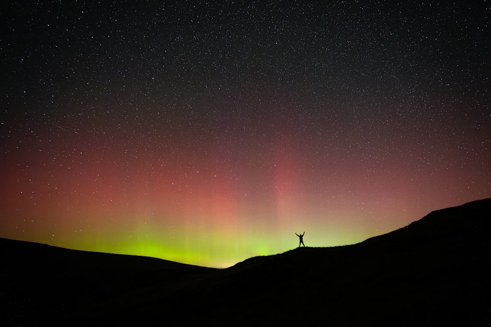 a person standing on top of a hill under a colorful sky