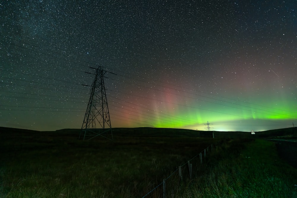 une aurore verte et rouge au-dessus d’un champ avec des lignes électriques