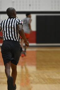 A referee signaling during a lively youth basketball game inside the gym.