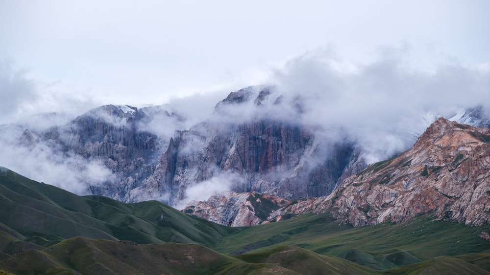 the mountains are covered in clouds and green grass