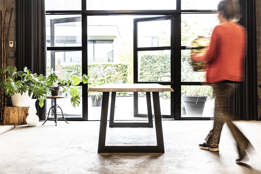 a woman walking past a table with a plant on it