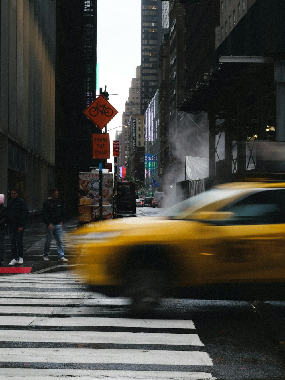 a yellow taxi driving down a street next to tall buildings