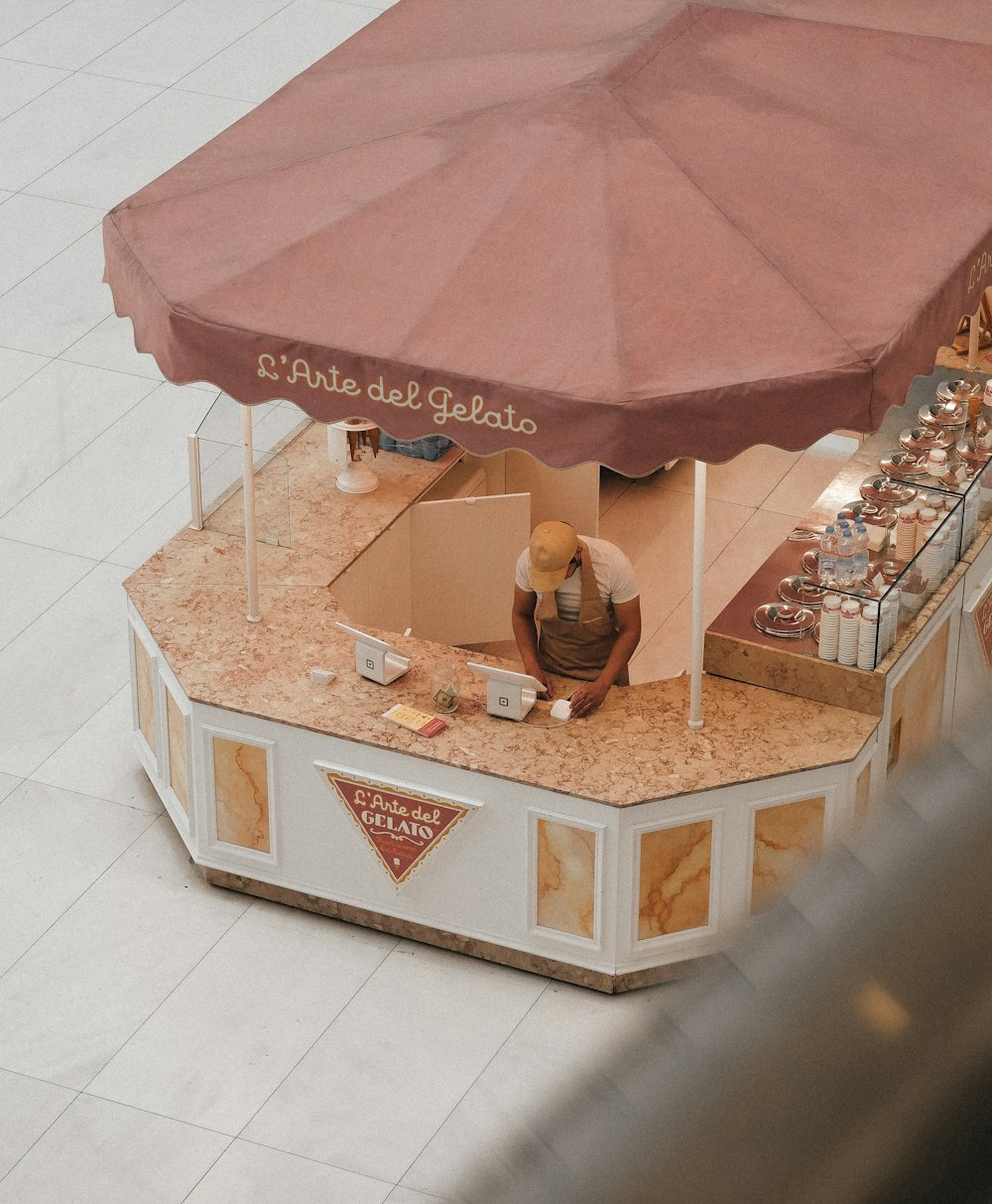 a food stand with a red umbrella and a man sitting at it
