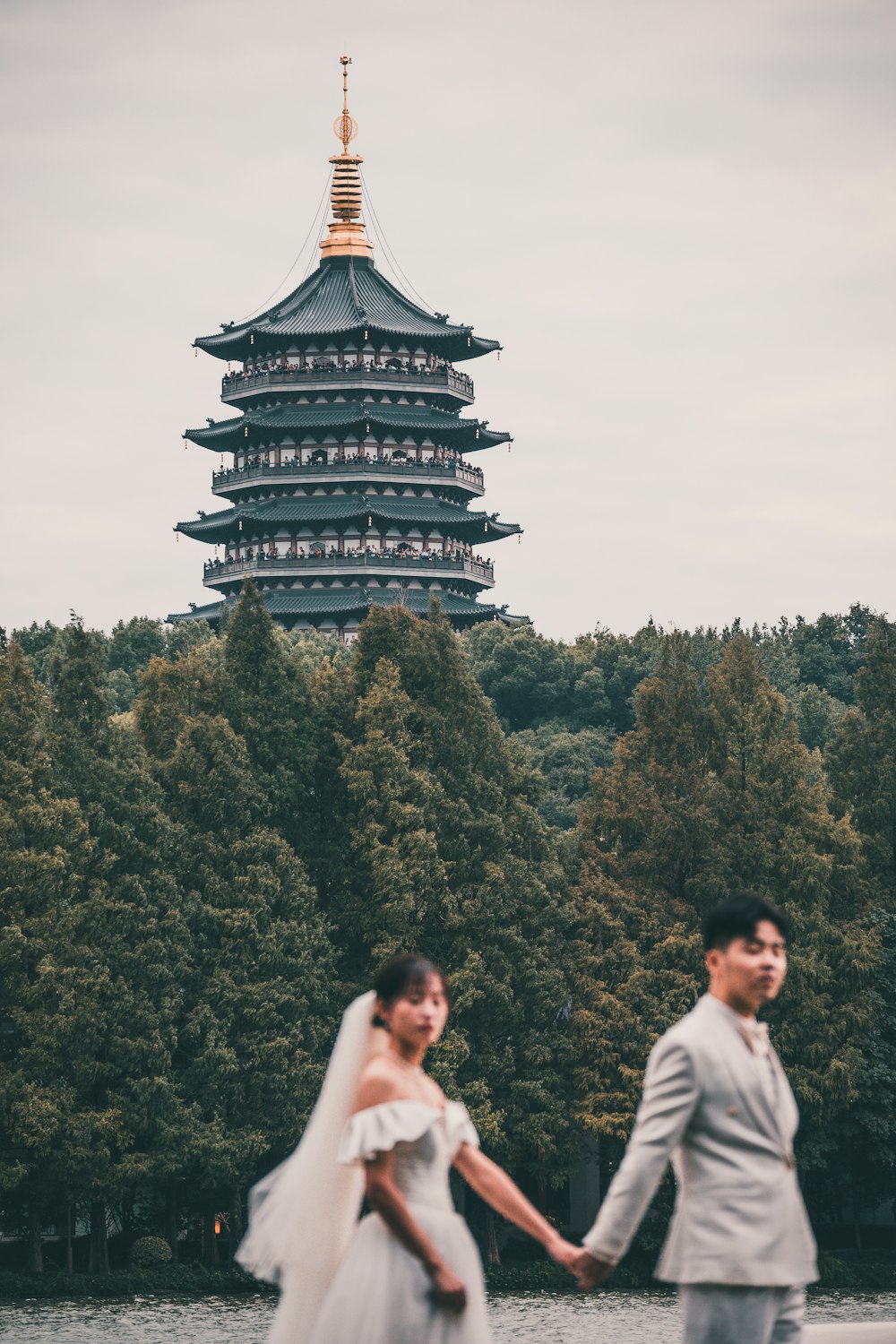 a bride and groom holding hands in front of a pagoda