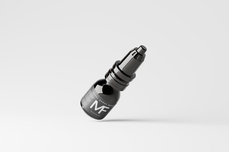 A dark-colored spray bottle with a sleek design is seen against a plain, light background. The bottle features a label with the letters 'MF' prominently displayed.