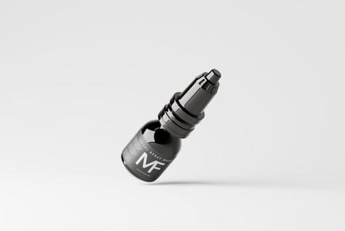 A dark-colored spray bottle with a sleek design is seen against a plain, light background. The bottle features a label with the letters 'MF' prominently displayed.