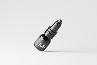 A dark-colored spray bottle with a sleek design is seen against a plain, light background. The bottle features a label with the letters 'MF' prominently displayed.