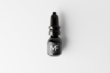 A black nasal spray bottle with a nozzle lid is placed against a light background. The label on the bottle features large, bold letters 'MF'. The design is sleek and minimalist, conveying a modern aesthetic.