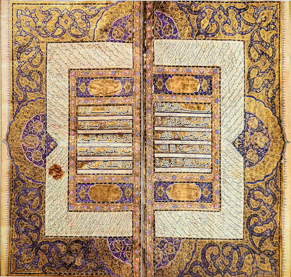 A close-up of an ancient manuscript page showing elegant Arabic calligraphy with delicate floral motifs in cream and brown hues.