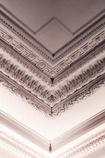 Intricately detailed architectural molding adorns the ceiling, featuring classical Greek or Roman motifs with decorative patterns and reliefs.