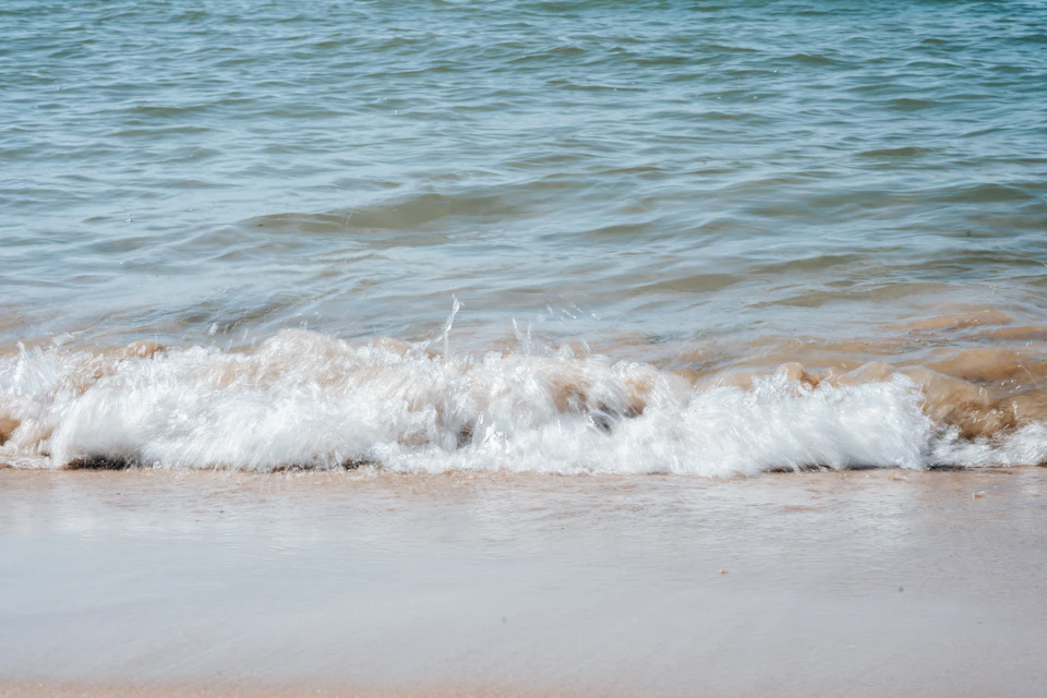 Serene beach scene features light beige sand and clear blue water with gentle waves