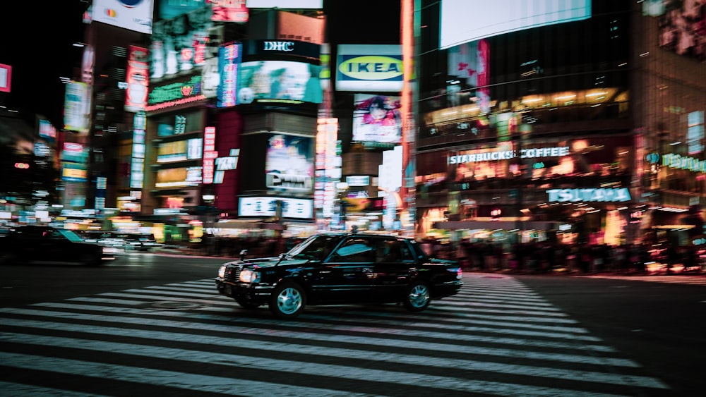 a black car driving down a street next to tall buildings