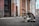 A tabby cat sits on a paved street lined with old buildings. The architecture features weathered wooden doors and faded walls, providing a rustic urban backdrop.