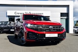 A bright red Volkswagen SUV is prominently displayed in front of a dealership with a sign reading 'Crewe Volkswagen.' The car has sleek black rims and a modern grill design, parked on a paved surface. Other vehicles are showcased in the background, contributing to a professional automotive setting.