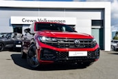 A bright red Volkswagen SUV is prominently displayed in front of a dealership with a sign reading 'Crewe Volkswagen.' The car has sleek black rims and a modern grill design, parked on a paved surface. Other vehicles are showcased in the background, contributing to a professional automotive setting.
