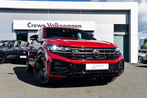 A bright red Volkswagen SUV is prominently displayed in front of a dealership with a sign reading 'Crewe Volkswagen.' The car has sleek black rims and a modern grill design, parked on a paved surface. Other vehicles are showcased in the background, contributing to a professional automotive setting.