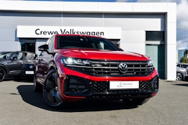 A bright red Volkswagen SUV is prominently displayed in front of a dealership with a sign reading 'Crewe Volkswagen.' The car has sleek black rims and a modern grill design, parked on a paved surface. Other vehicles are showcased in the background, contributing to a professional automotive setting.