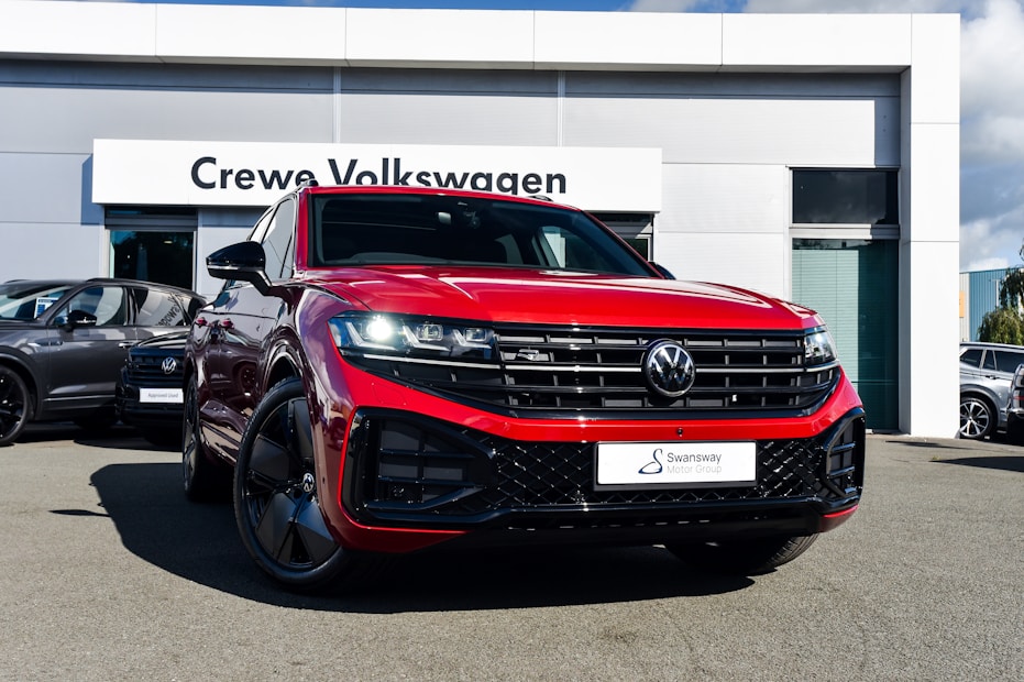 A bright red Volkswagen SUV is prominently displayed in front of a dealership with a sign reading 'Crewe Volkswagen.' The car has sleek black rims and a modern grill design, parked on a paved surface. Other vehicles are showcased in the background, contributing to a professional automotive setting.