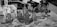 A collection of clear and intricately designed glass bottles and vases displayed on a table. Around the glassware, there are also cardboard boxes containing sets of glassware, possibly champagne flutes. The setting is outdoors, possibly at a market or a display area.