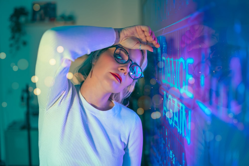 a woman wearing glasses leaning against a wall