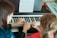A person is teaching a child how to play the piano, with sheet music placed on top of the piano. The hands of the adult are gently guiding the child's fingers over the keys.
