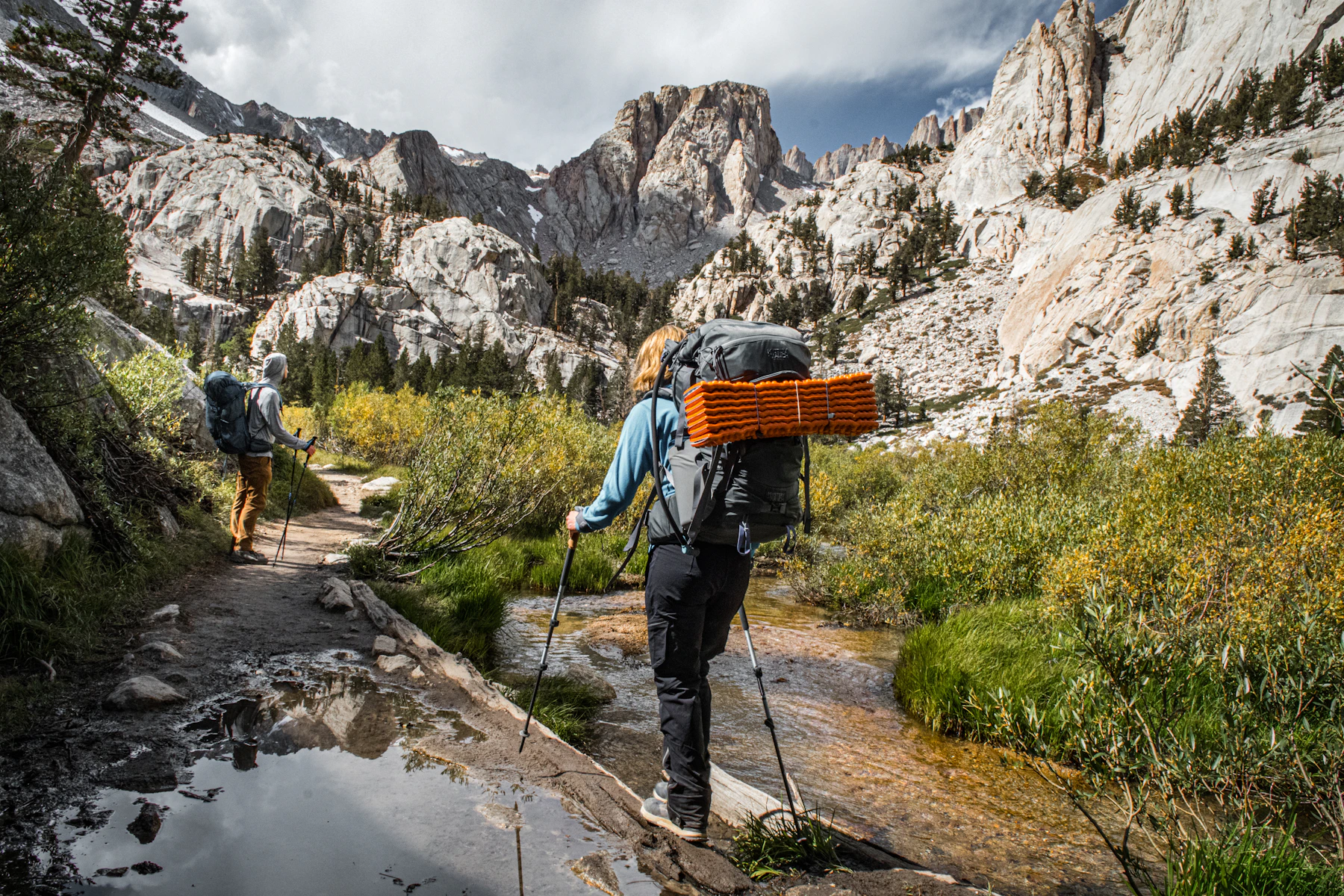 Backpackers carrying outdoor equipment along a rocky mountain trail