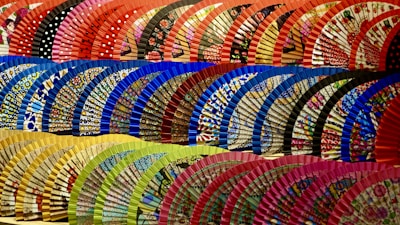 Hand fans made from African prints displayed in a rustic basket, highlighting their bold colors and craftsmanship.