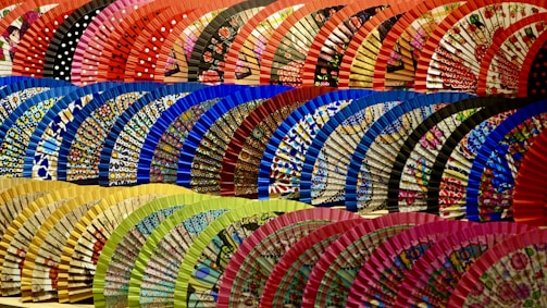A collection of African print hand fans arranged in a fan shape, each with bold, colorful patterns.