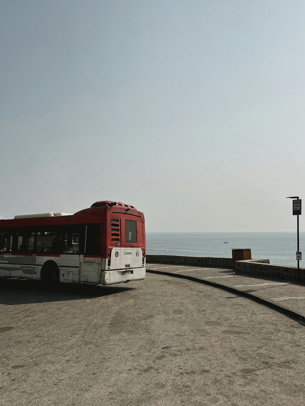 a red and white bus parked next to the ocean