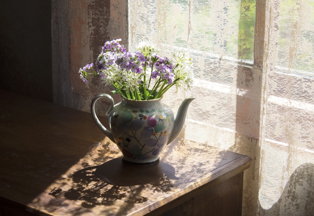 a teapot filled with purple flowers sitting on a window sill