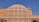 An ornate, multi-level palace facade with a series of intricately carved pink sandstone windows, traditional in Rajasthani architecture. Symmetrical design with hundreds of small windows decorated with elaborate latticework, against a clear blue sky.