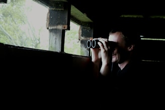A private investigator using binoculars from a concealed location during a surveillance operation.