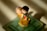 A small figurine of a boy and a girl embracing, with the boy holding a red rose. The figurine is positioned on a square green base, and light casts soft shadows around it. The girl has a purple hat and wears a yellow dress, while the boy is dressed in dark clothing.