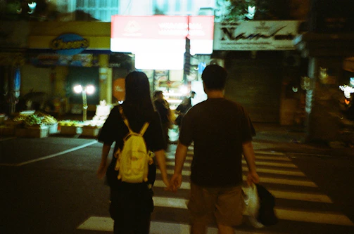 An intimate candid of a couple holding hands walking through a softly lit urban street at dusk.