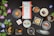 An assortment of traditional Japanese sweets artistically arranged on a dark, textured surface. Each sweet is placed in a unique dish, ranging from round and square plates to leaf-shaped trays. Vibrant artificial morning glory flowers with green leaves accentuate the setup. In the center, a wrapped gift box tied with a ribbon suggests a special occasion. Nearby, a card with Japanese text and a logo complements the arrangement. The scene combines delicacies like a roll cake, colorful dango, and various pastries, reflecting a diverse culinary display.