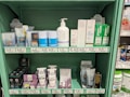 A store shelf filled with various health and wellness products, including lotions, creams, and lip balms. The shelf features brands like Charlotte's Web, Social, Joy, and Green Roads. Products are labeled with prices and organized neatly by brand. The shelf is painted in a light green color, complementing the packaging design of many products.