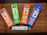 Four CBD vape pen boxes are arranged on a wooden surface. Each box is brightly colored, featuring different flavors: Strawberry Lemonade, Fresh Mint, Tropic Breeze, and Blue Raspberry. The boxes indicate 500mg of CBD per pen. A single white vape pen with the CBD logo lies horizontally below the boxes.