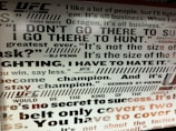 A wall filled with motivational quotes associated with the UFC. The text includes statements from notable individuals like Dana White, BJ Penn, and Georges St-Pierre, emphasizing themes of competition, strength, and success. The typography is bold and varied in size, with a mixture of black, gray, and some red on a white background.