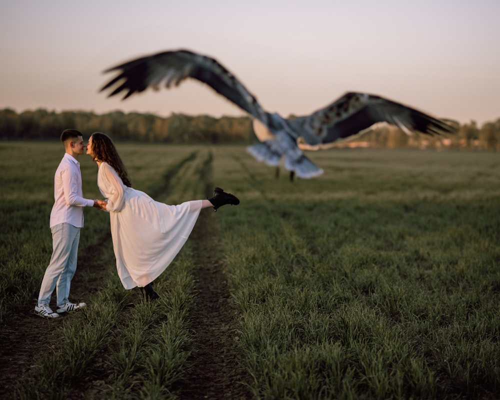 a man and a woman standing in a field with a bird flying overhead